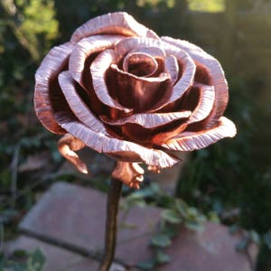 May include: A copper rose sculpture with a detailed, realistic design. The rose is a single bloom with a long stem and is finished in a warm, copper color.