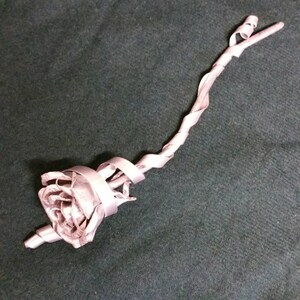 May include: A silver metal rose with a twisted stem. The rose is made of thin metal strips that are twisted and curled to create the shape of a rose.