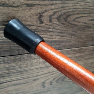 Pu&ograve; includere: Primo piano di un bastone da passeggio in legno con una punta in gomma nera. Il bastone &egrave; di colore marrone rossiccio e ha una finitura liscia.