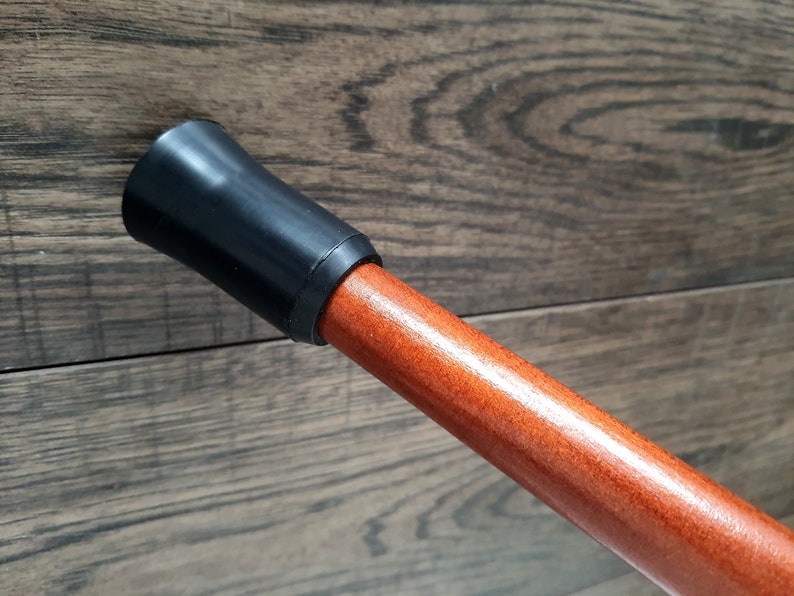 Pu&ograve; includere: Primo piano di un bastone da passeggio in legno con una punta in gomma nera. Il bastone &egrave; di colore marrone rossiccio e ha una finitura liscia.