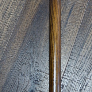 Puede incluir: Un bast&oacute;n de madera con un tinte marr&oacute;n y una banda de metal dorado con un dise&ntilde;o trenzado.