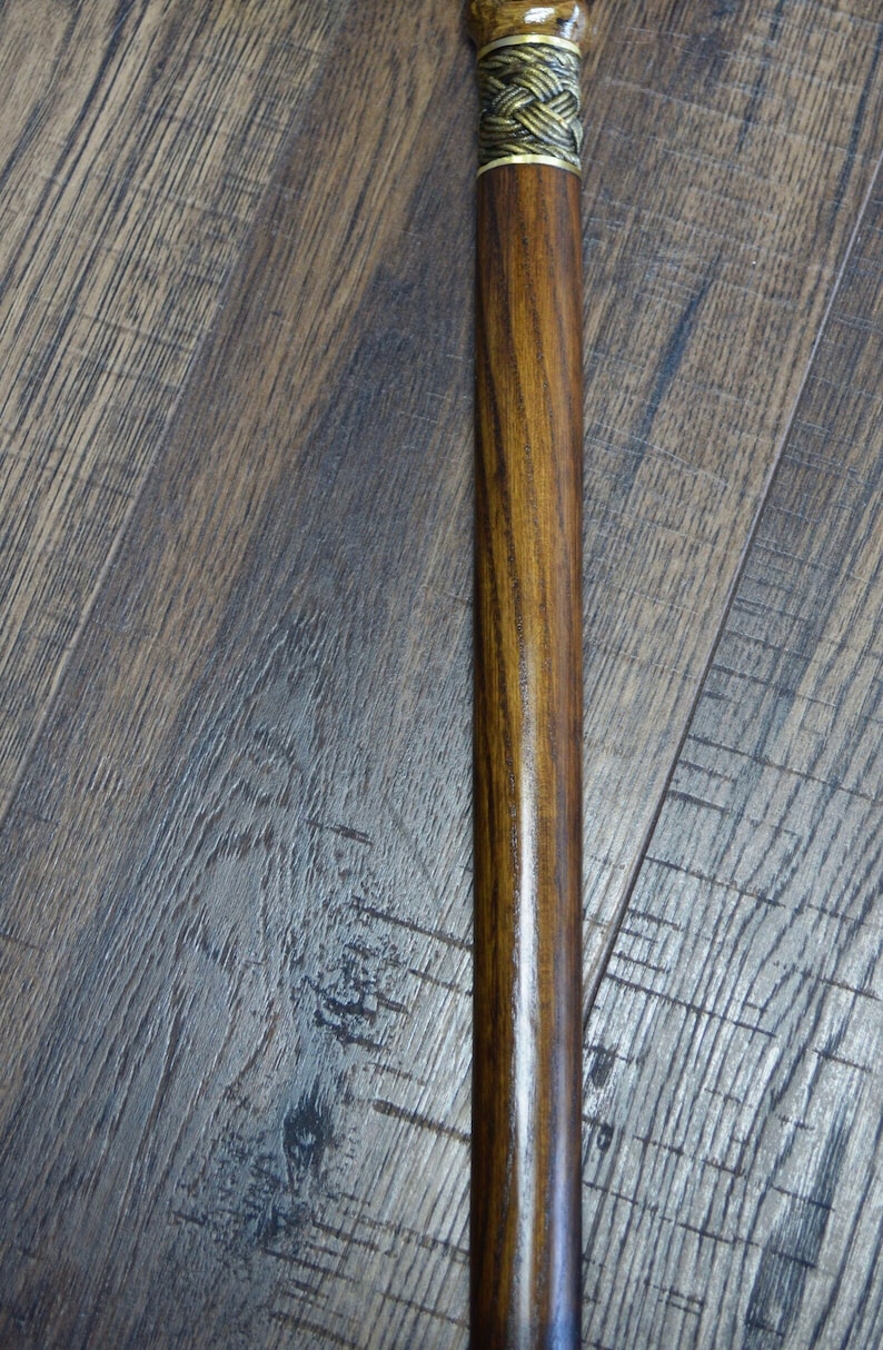 Puede incluir: Un bast&oacute;n de madera con un tinte marr&oacute;n y una banda de metal dorado con un dise&ntilde;o trenzado.