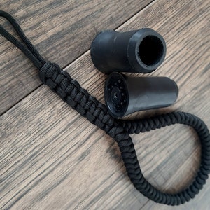 Pu&ograve; includere: Cordino in paracord nero con due punte in gomma nera per bastoni da trekking. Le punte hanno una superficie testurizzata e un foro al centro.