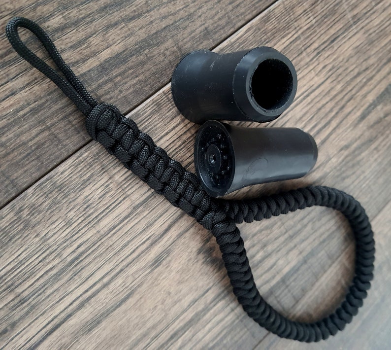 Pu&ograve; includere: Cordino in paracord nero con due punte in gomma nera per bastoni da trekking. Le punte hanno una superficie testurizzata e un foro al centro.