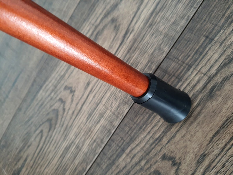 Pu&ograve; includere: Primo piano di un bastone da passeggio in legno con una punta in gomma nera. Il bastone &egrave; marrone e ha una finitura liscia.