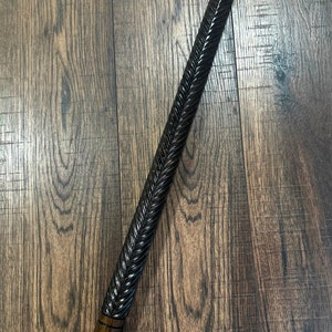 Puede incluir: Un bast&oacute;n de madera con un acabado marr&oacute;n oscuro y un dise&ntilde;o tallado. El bast&oacute;n tiene una parte superior de metal con un dise&ntilde;o decorativo.