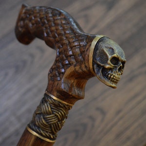 Puede incluir: Un bast&oacute;n de madera con un dise&ntilde;o tallado detallado y un mango en forma de calavera. El mango es de metal y tiene un acabado dorado.