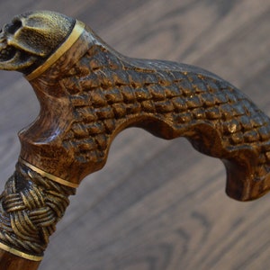 Puede incluir: Un bast&oacute;n de madera con un mango en forma de calavera. El mango est&aacute; tallado con un dise&ntilde;o de calavera detallado y tiene detalles dorados. El eje del bast&oacute;n es de madera marr&oacute;n con un dise&ntilde;o trenzado dorado.
