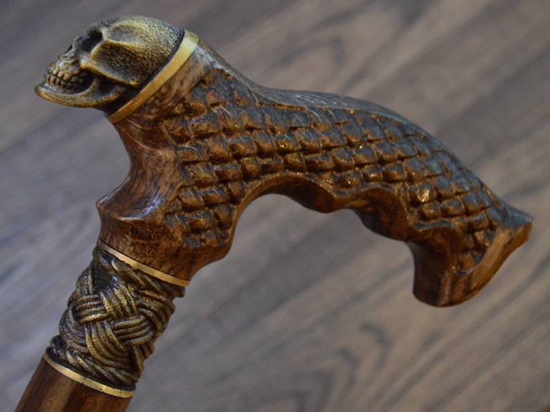 Puede incluir: Un bast&oacute;n de madera con un mango en forma de calavera. El mango est&aacute; tallado con un dise&ntilde;o de calavera detallado y tiene detalles dorados. El eje del bast&oacute;n es de madera marr&oacute;n con un dise&ntilde;o trenzado dorado.