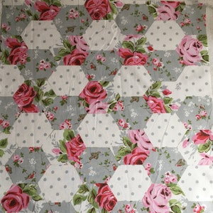 May include: A patchwork fabric featuring a repeating pattern of gray and white hexagons with a floral design. The floral design features pink roses, green leaves, and small white flowers. The hexagons are arranged in a staggered pattern.