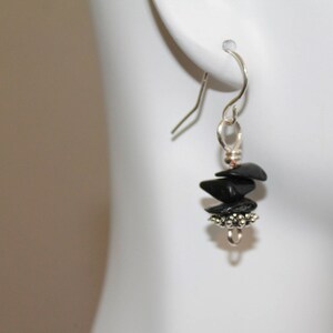 May include: Black gemstone earrings with silver accents. The earrings are dangle style and feature a cluster of black stones.