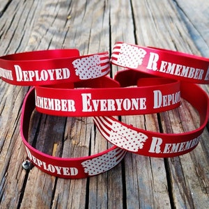 May include: Red silicone bracelets with white text and a white American flag design. The text on the bracelets reads "Remember Everyone Deployed".