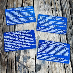 May include: Four blue cards with white text outlining the Miranda Warning, Implied Consent Warning, Pirtle Warning, and Implied Consent Warning for Fatal or Serious Bodily Injury Crash. The cards are on a wooden surface.