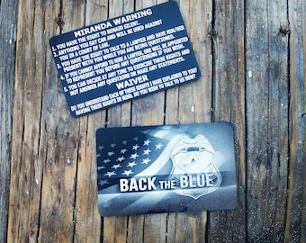 May include: A black and white card with the text "Miranda Warning" and a list of rights. The card also has a black and white image of a police badge and the text "Back the Blue".