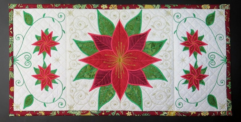 Op de afbeelding: Een witte gestikte tafelrunner met een rood kerstster-ontwerp en groene bladeren. De runner heeft een gouden en rode rand.