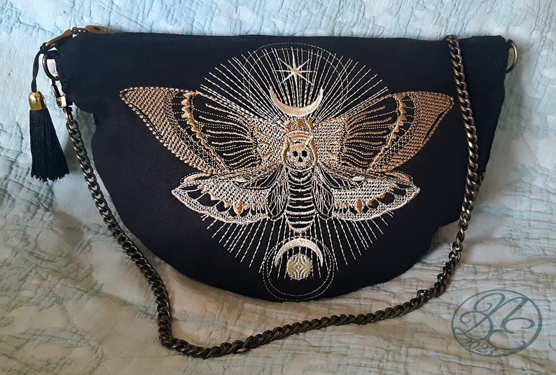 May include: A black fabric handbag with a gold chain strap and a gold embroidered moth design. The moth has a crescent moon and star above it.