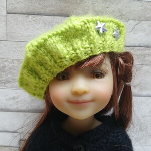 Peut inclure: Un béret tricoté vert citron avec deux étoiles argentées. Le béret est porté par une poupée aux cheveux bruns et un pull noir. Le béret est un accessoire élégant.