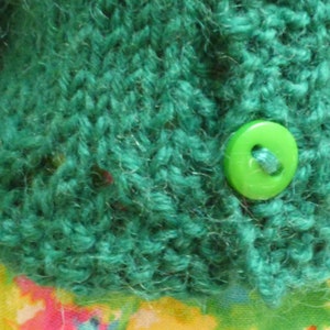 May include: A teal green knitted cardigan with a lime green button.