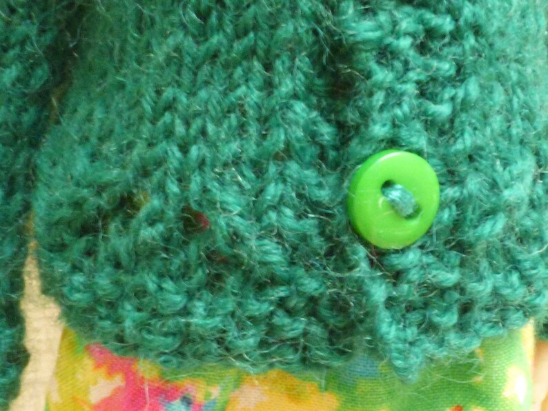 May include: A teal green knitted cardigan with a lime green button.