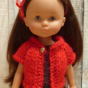 May include: A red knitted cardigan with a button closure, worn by a doll with long brown hair and a red headband.