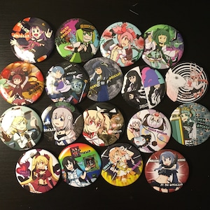 Puede incluir: Una colección de 18 botones redondos coloridos con personajes de anime y el texto "Digi Onigiri". Los botones están dispuestos en círculo sobre una superficie negra.