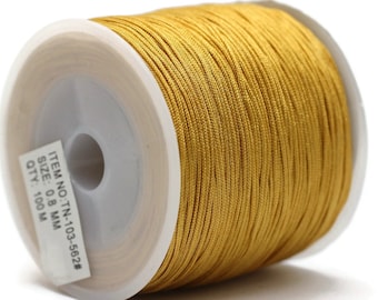 May include: A spool of golden-yellow cord, tightly wound on a white plastic core. The cord is 0.8 mm in size and is labeled with item number TN-103-562#. The spool is against a white background.
