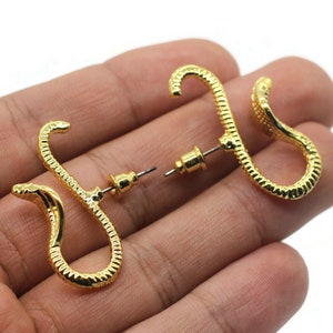 May include: A pair of gold snake-shaped earrings. The earrings are made of a textured metal and have a simple post back.