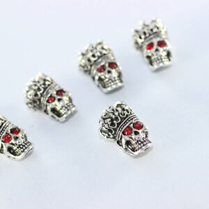 May include: Five silver skull charms with red gem eyes and a crown on top.