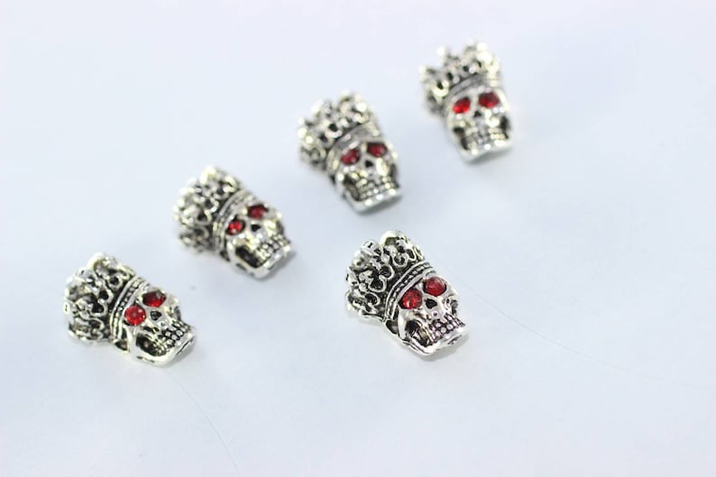 May include: Five silver skull charms with red gem eyes and a crown on top.