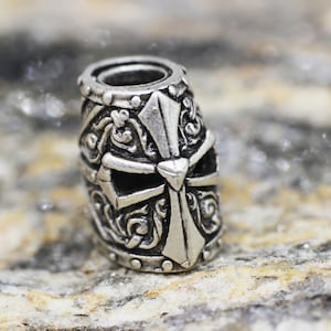 May include: Silver charm with a detailed design of a knight's helmet with a cross on the front.