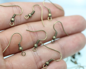 May include: A close-up of a hand holding several bronze-colored earring hooks. The hooks have a spring-loaded closure and a small ball at the top.