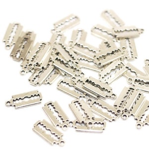 May include: A pile of silver-toned metal razor blade charms. The charms are shaped like a razor blade with a small loop at the top for attaching to a chain or bracelet.