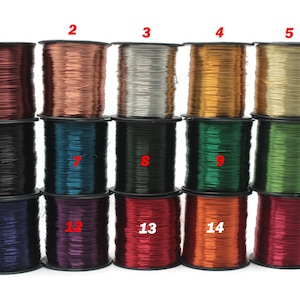 May include: A collection of fifteen spools of metallic craft wire in various colors, including shades of red, copper, gold, green, and black. The spools are stacked in rows, showcasing the range of colors available for jewelry making and crafting projects.