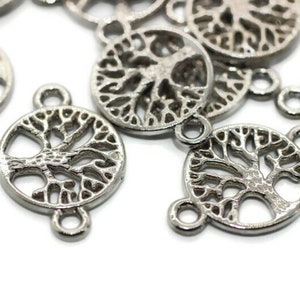 Op de afbeelding: Een close-up van zilverkleurige metalen bedels in de vorm van een levensboom. De bedels hebben drie lussen om aan sieraden of andere knutselprojecten te bevestigen.