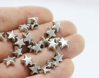 Könnte beinhalten: Nahaufnahme einer Hand, die einen Haufen silberner, sternförmiger Metall-Anhänger hält. Die Anhänger sind klein und haben eine glänzende Oberfläche.