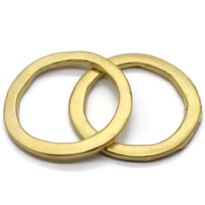 Puede incluir: Dos anillos de metal de color dorado entrelazados. Los anillos son lisos y tienen una forma ligeramente irregular.