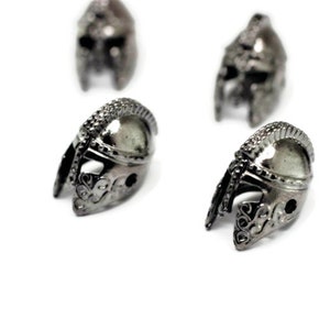 May include: Four silver-colored metal helmet charms with intricate details. The helmets are all facing the same direction and are arranged in a semi-circle.