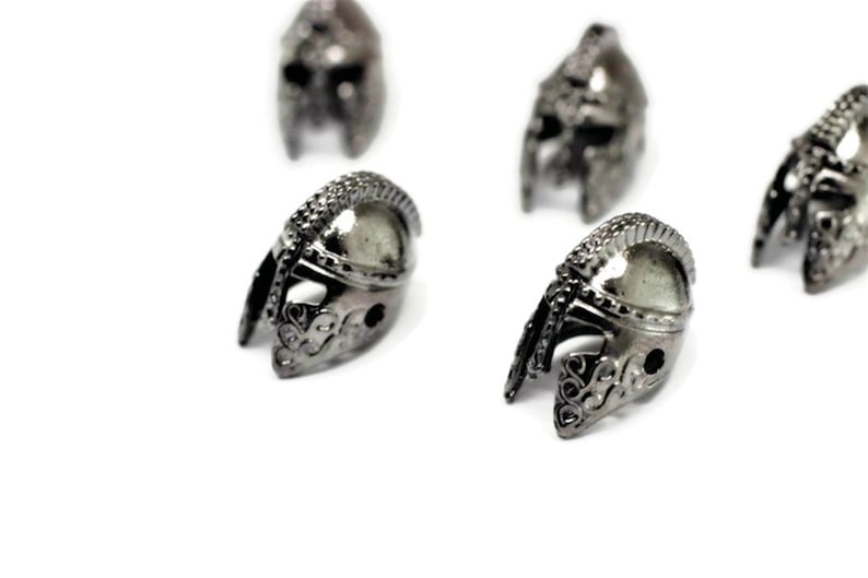 May include: Four silver-colored metal helmet charms with intricate details. The helmets are all facing the same direction and are arranged in a semi-circle.