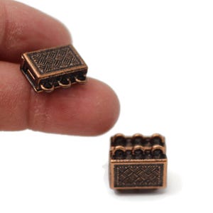 May include: Two antique copper-toned metal clasps with a decorative pattern. Each clasp has three loops for attaching jewelry.