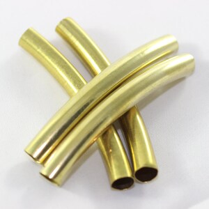 Puede incluir: Cuatro tubos de metal de color dorado, cada uno doblado en una curva suave. Los tubos est&aacute;n dispuestos en forma de cruz.