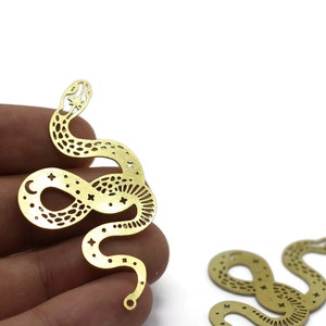 May include: Two gold metal snake charms with a cutout design featuring stars and a crescent moon. The charms are perfect for jewelry making or crafting.
