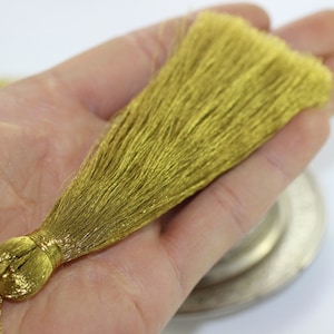 Może przedstawiać: Złoty frędzl z długim, płynnym frędzlem. Frędzl jest przymocowany do sznurka i idealnie nadaje się do dodania odrobiny elegancji do każdego projektu.