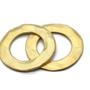 Op de afbeelding: Twee gouden metalen ringen met een gehamerde textuur. De ringen zijn in elkaar gehaakt.