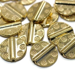May include: A group of gold-colored metal beads with a textured surface and a raised line across the center. The beads are round and have a hole in the center for stringing.