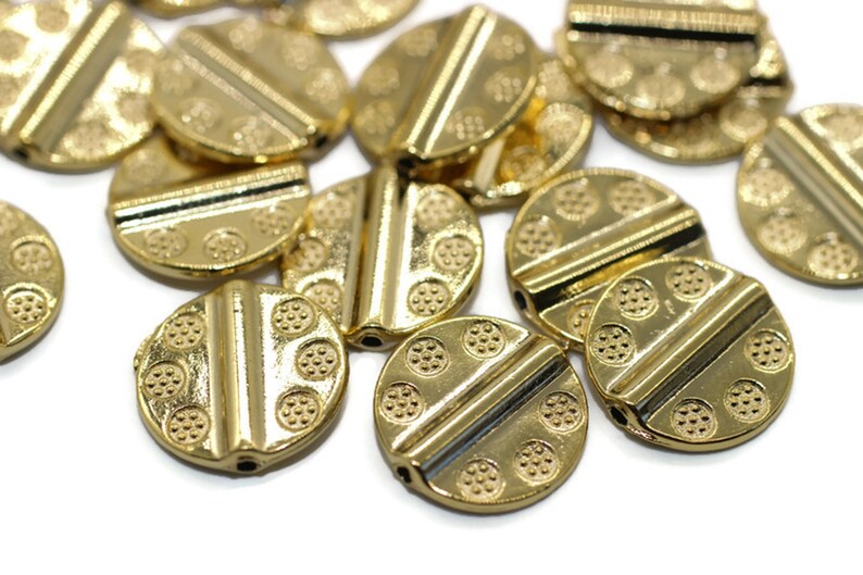 May include: A group of gold-colored metal beads with a textured surface and a raised line across the center. The beads are round and have a hole in the center for stringing.