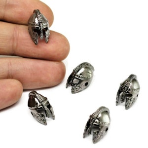May include: Four silver-toned metal helmet charms with intricate details. The charms are small and have a textured surface.