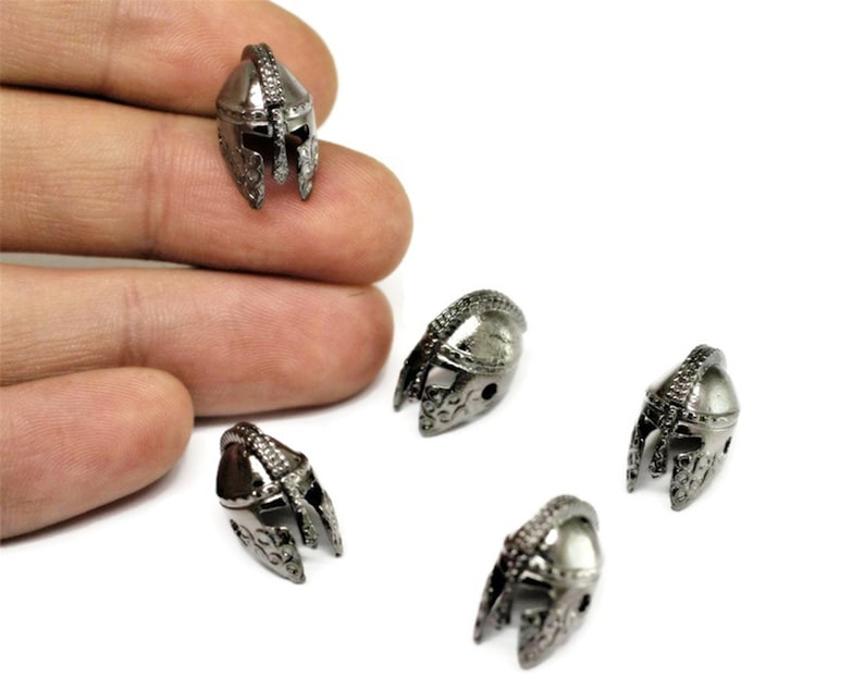 May include: Four silver-toned metal helmet charms with intricate details. The charms are small and have a textured surface.