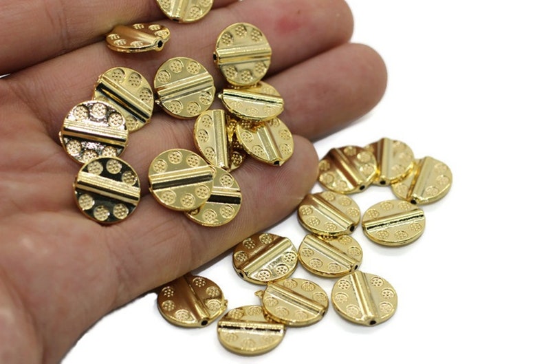 May include: A collection of gold-toned metal beads with a textured surface and a raised line across the center. The beads are round and have a hole in the center for stringing.