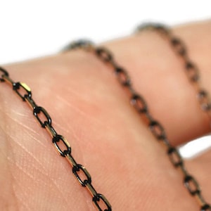 May include: A close-up of a black chain with gold accents. The chain is made of small, linked oval shapes.