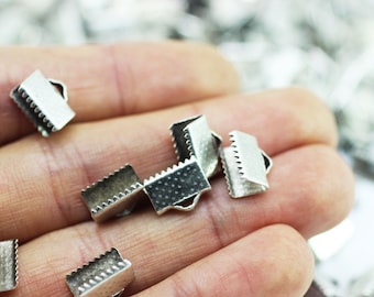 Op de afbeelding: Een close-up van een hand die verschillende zilveren metalen sluitingen vasthoudt. De sluitingen zijn klein en hebben een decoratief ontwerp.